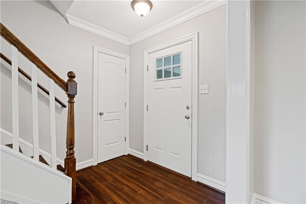 Entry foyer with dark hardwood floors, a white front door, and a staircase with a dark wood handrail.