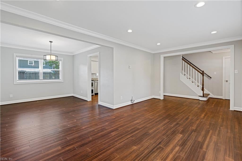 Vacant living room with dark hardwood floors, a large window, and an open view of the staircase.