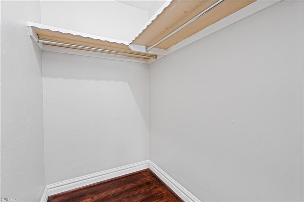 Empty closet with dark hardwood flooring and exposed wooden upper shelving.