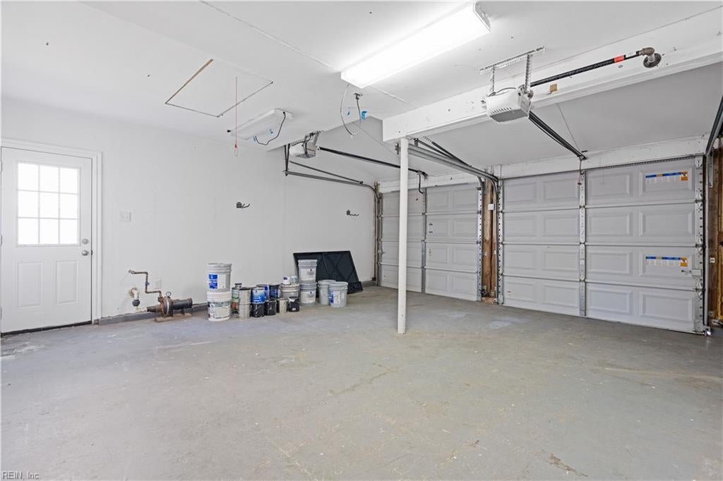 Spacious garage with two overhead doors, a side entry door, and paint cans along the wall.