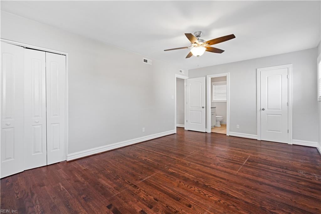 Empty bedroom with dark hardwood floors, double closet doors, and a ceiling fan.