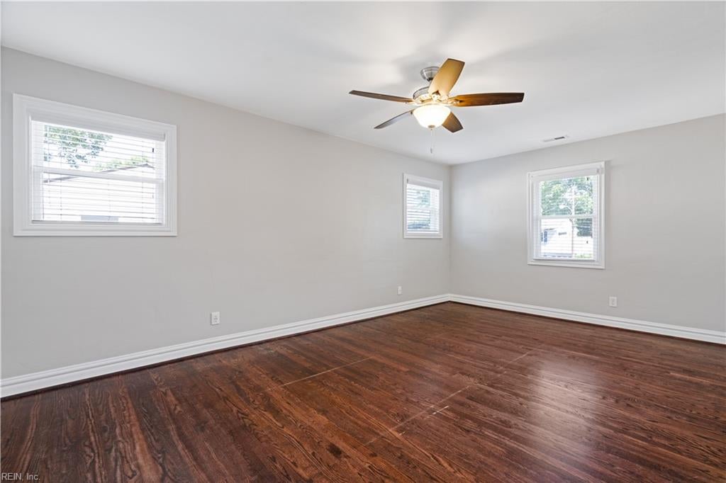 Empty room with dark hardwood floors, three windows, and a ceiling fan.