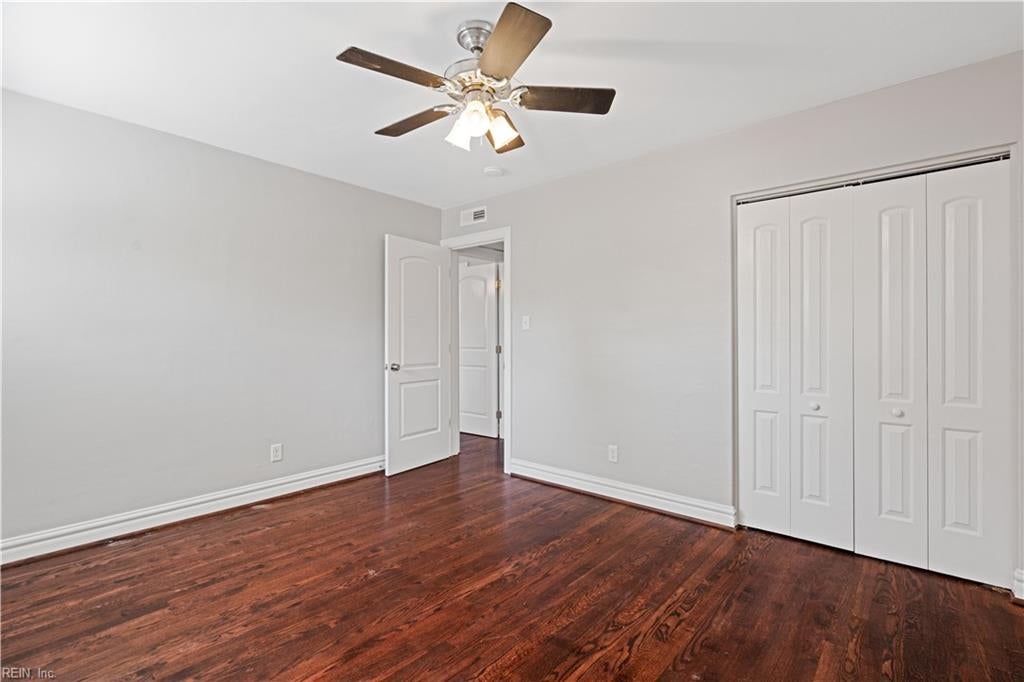 Empty bedroom with reddish hardwood floors, a ceiling fan, and white double closet doors.