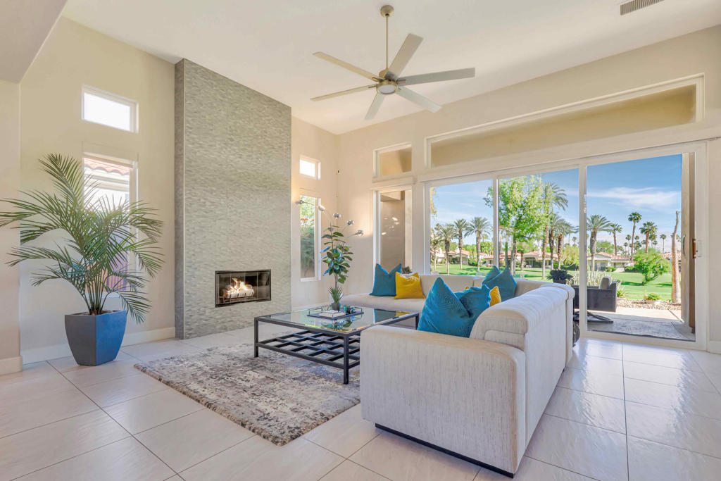 Living room with a tall stone fireplace and sliding doors overlooking a palm-lined golf course.