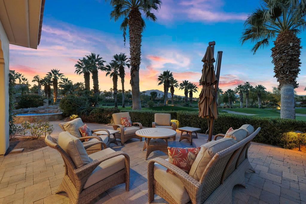 Furnished patio with wicker seating overlooks a palm-lined lawn at sunset.