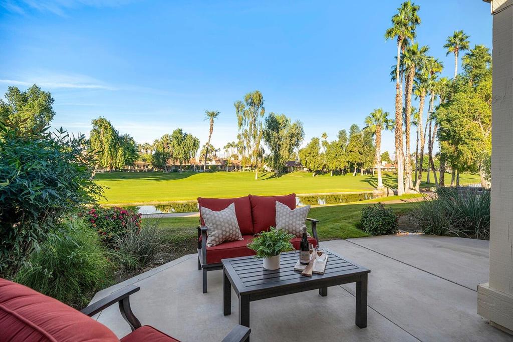 Patio seating overlooks a golf course, pond, and palm-lined fairway.