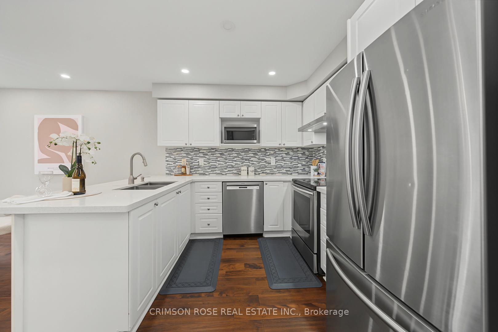 White kitchen with stainless steel appliances, mosaic backsplash, and dark wood flooring.