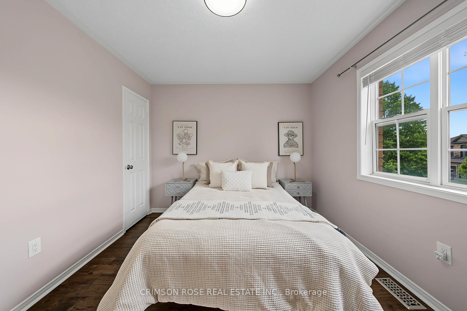 Staged bedroom with a neatly made bed, matching bedside tables, and a large window overlooking trees.