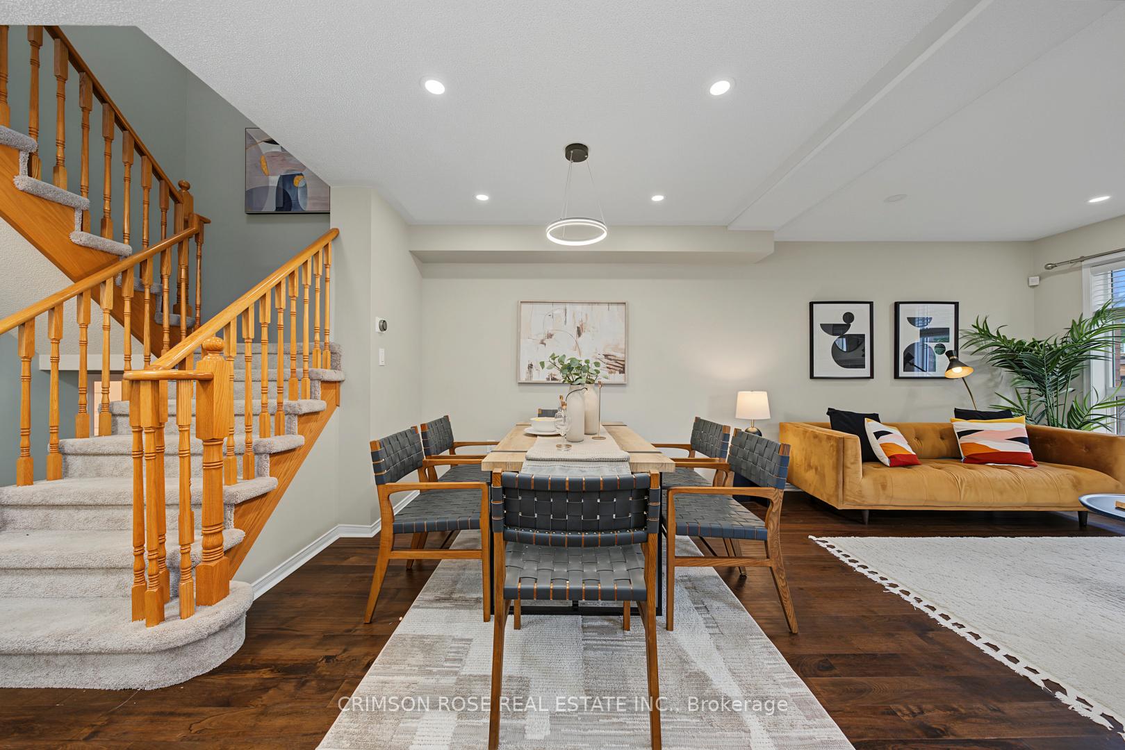 Staged dining and living area with a carpeted staircase, woven chairs, and mustard-colored sofa.