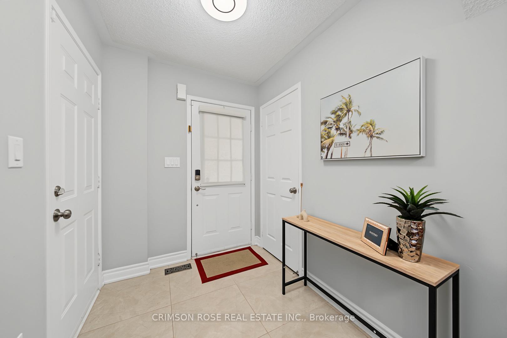 Bright staged entryway with white doors, tiled floor, console table, and palm-tree wall art.