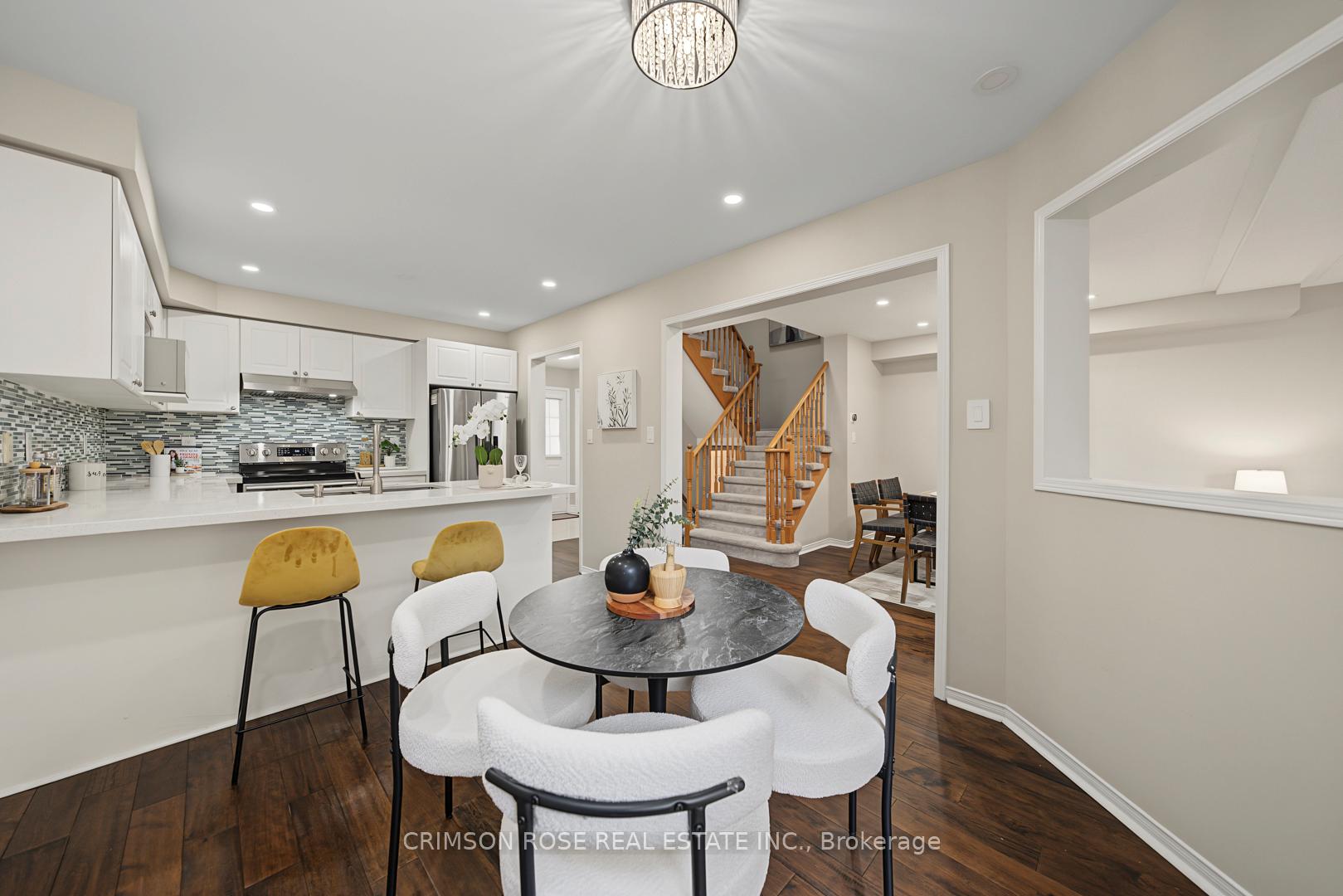 Open-plan kitchen and dining area with a mosaic backsplash, breakfast bar, and carpeted staircase.