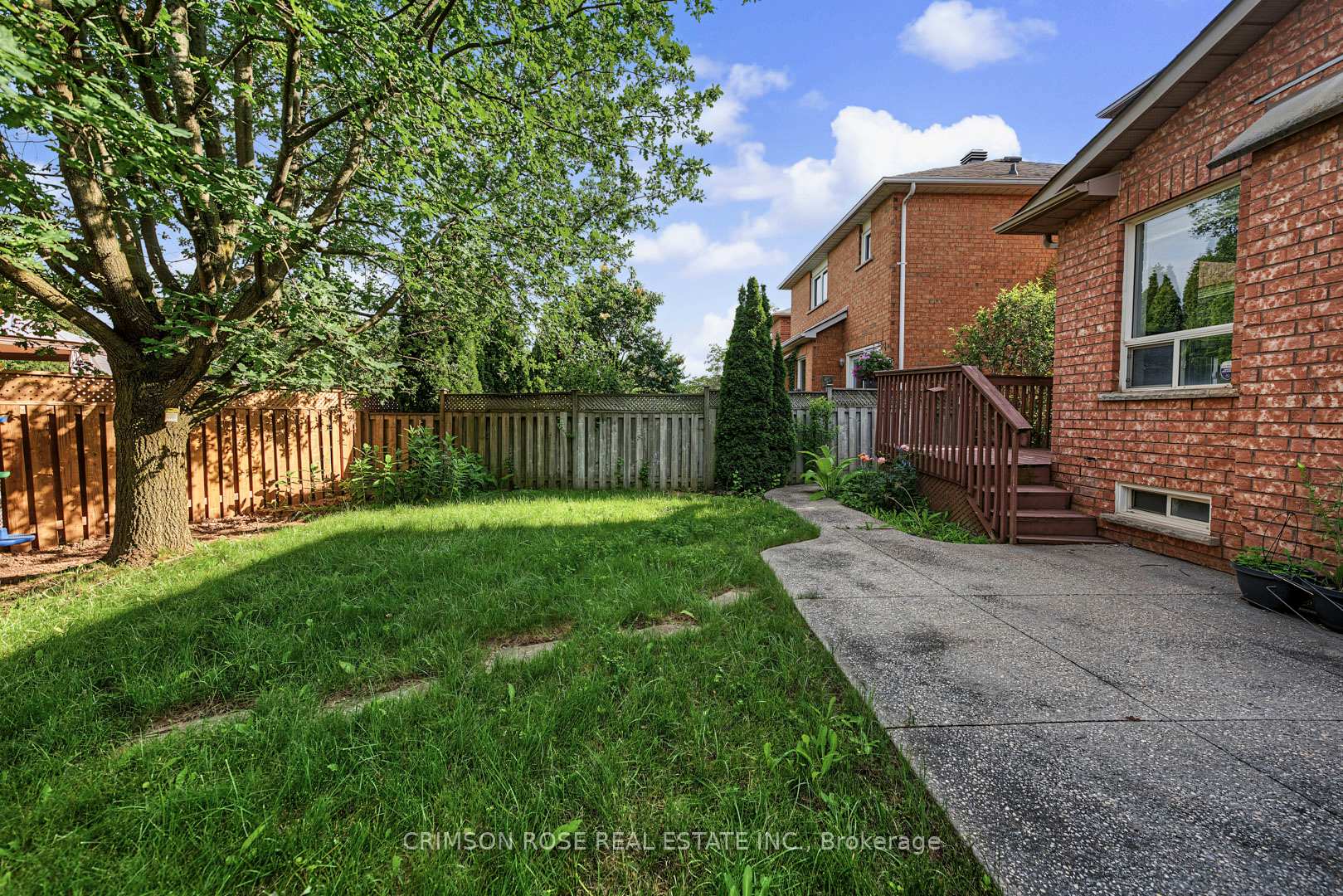 Backyard with a broad lawn, mature tree, fenced yard, and concrete patio beside a red-brick house.