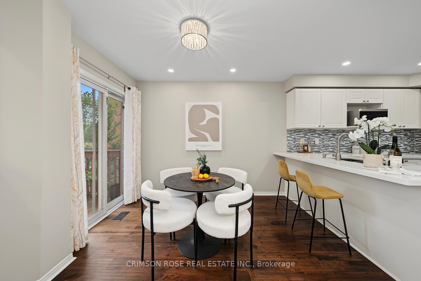 Dining area beside a white kitchen, with a round table, upholstered chairs, and sliding doors to a deck.