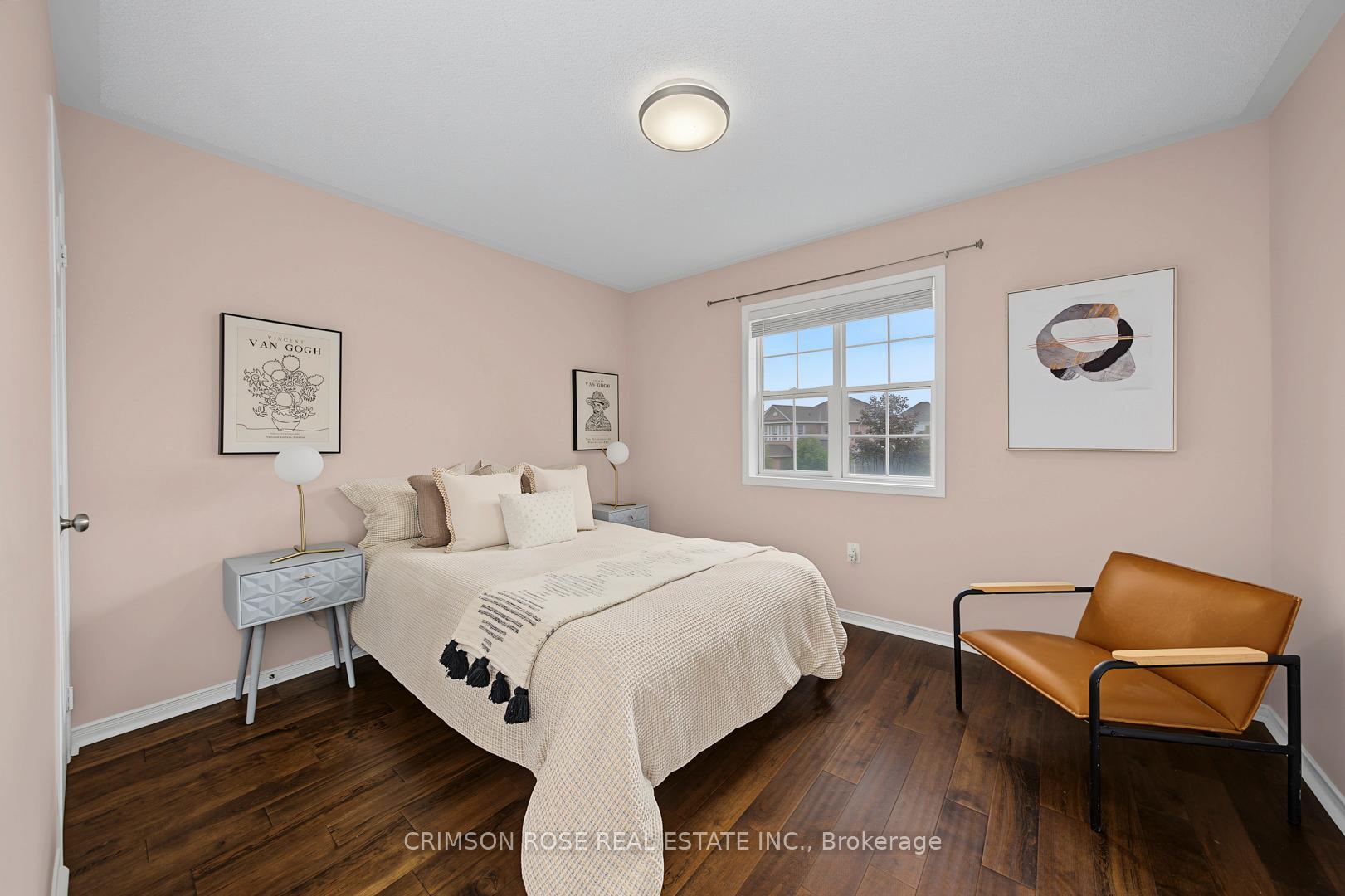 Staged bedroom with a cream bed, blush-pink walls, dark wood floors, and a tan leather chair.