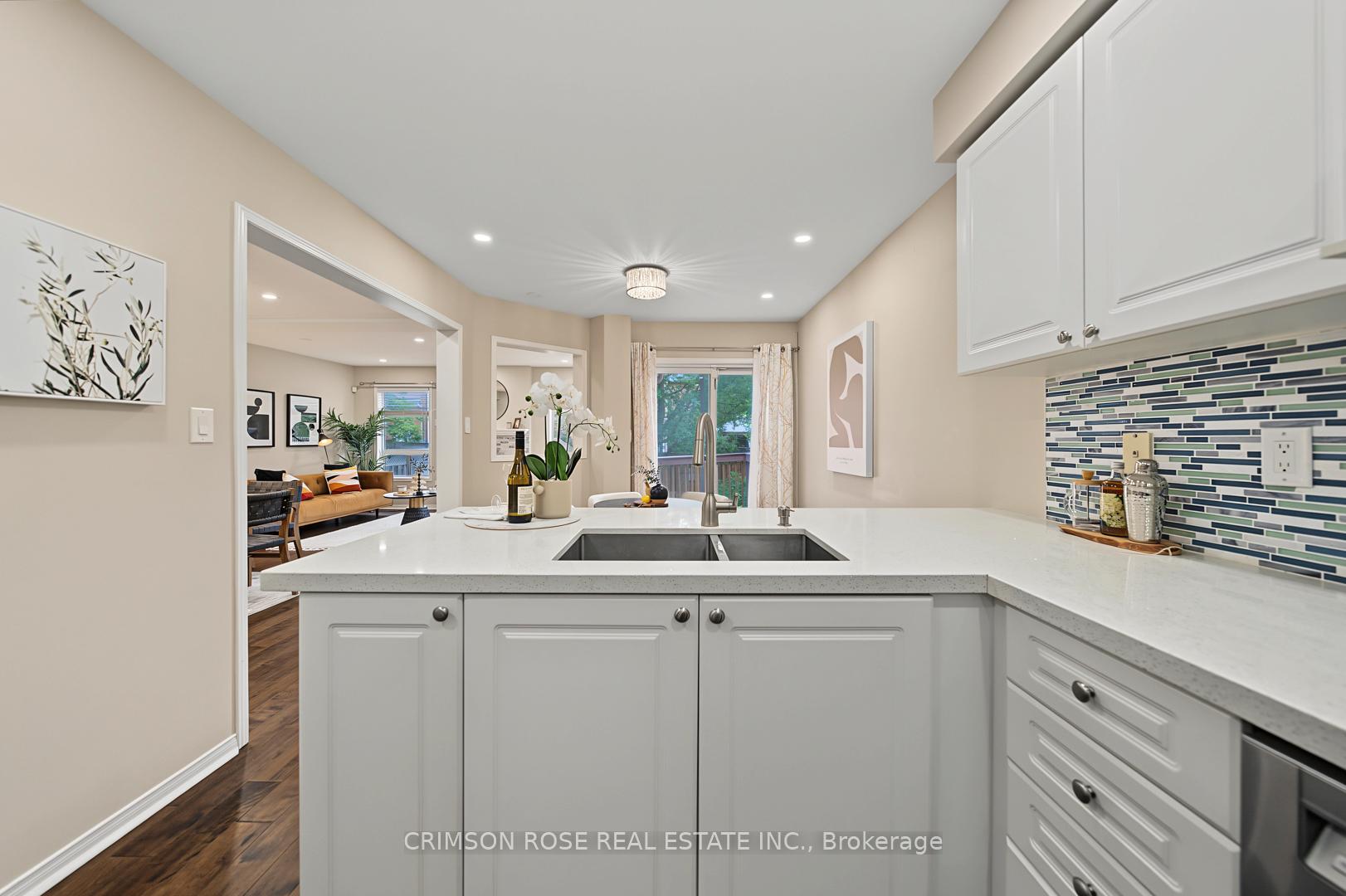 Bright kitchen with white cabinets, a broad sink peninsula, colorful tile backsplash, and a view into the living room.