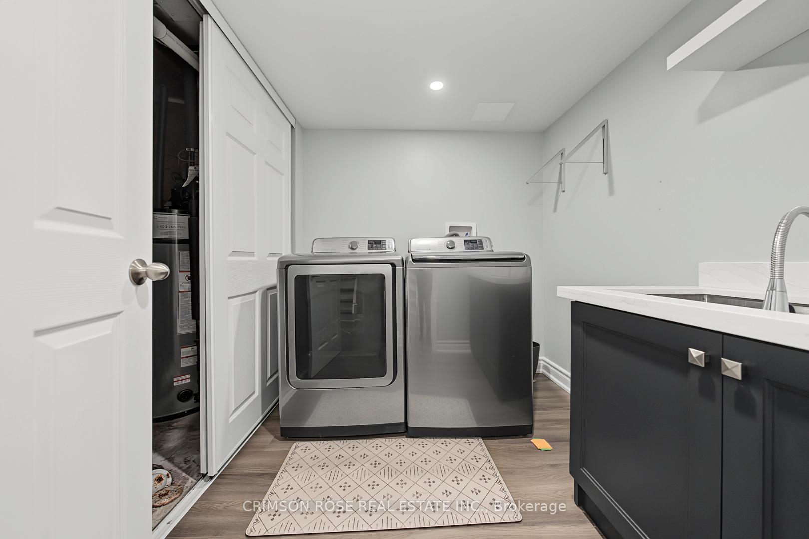 Laundry room with stainless washer and dryer, dark sink cabinetry, and an open water heater closet.
