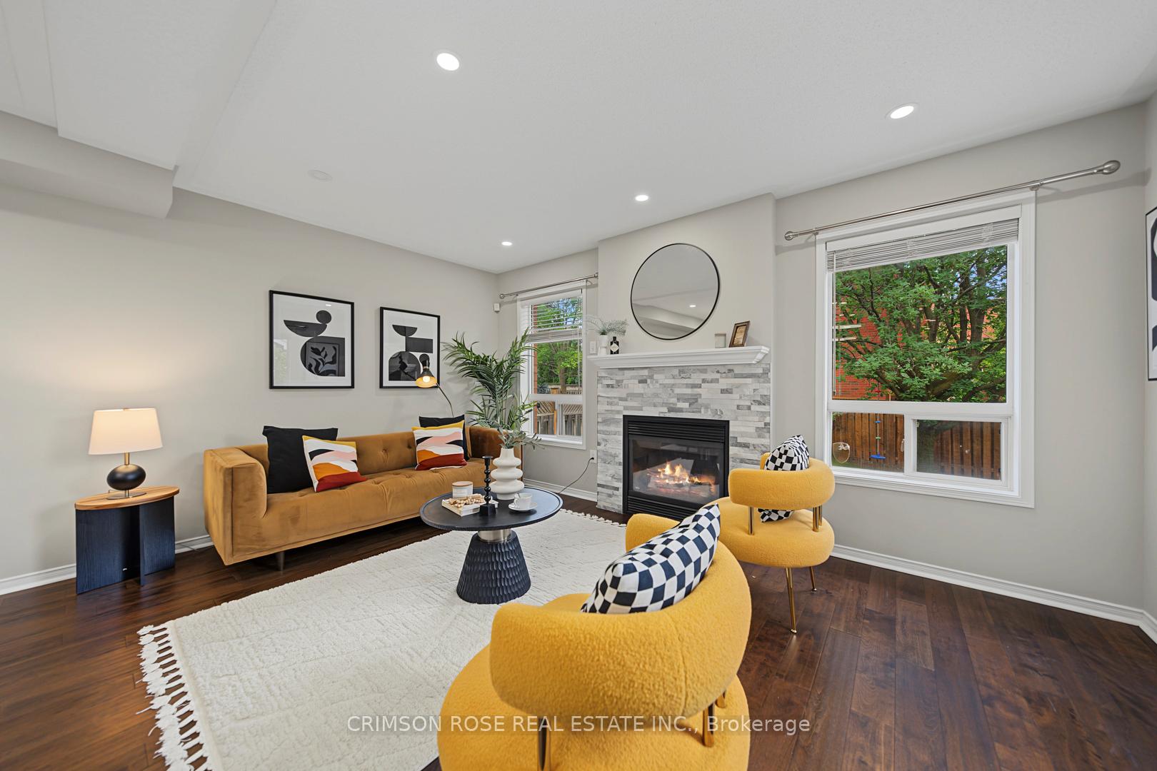 Staged living room with a stone-tiled fireplace, mustard seating, and large windows overlooking greenery.