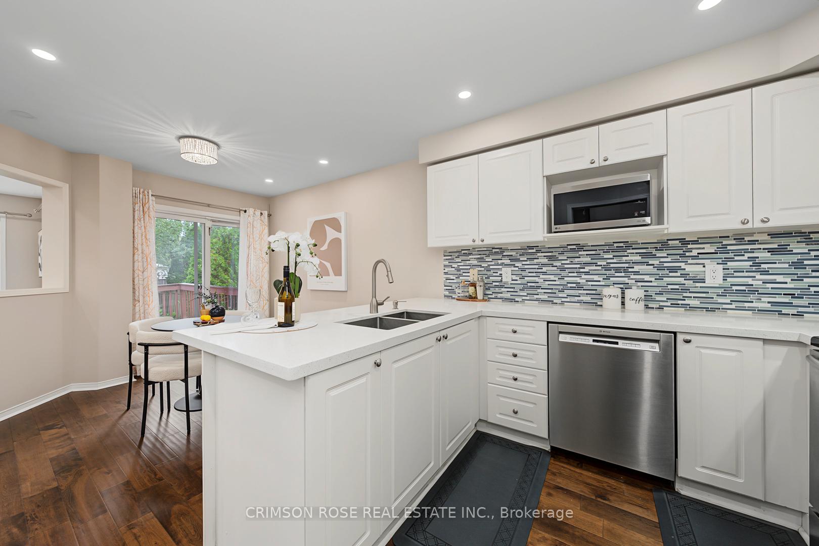 Bright white kitchen with a large peninsula, blue mosaic backsplash, stainless appliances, and sliding doors to a deck.