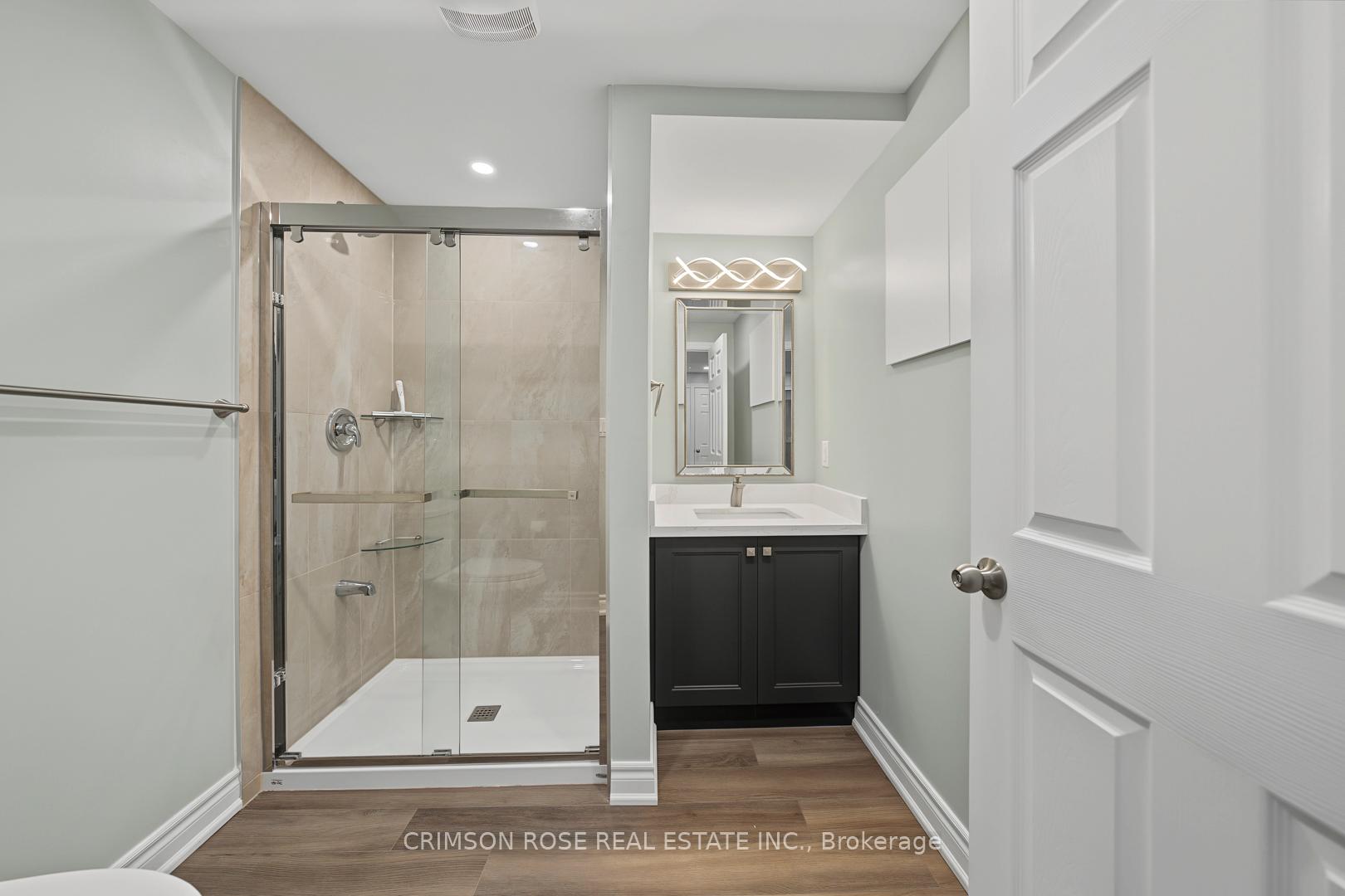 Modern bathroom with a glass-enclosed beige-tile shower and dark vanity with white countertop.