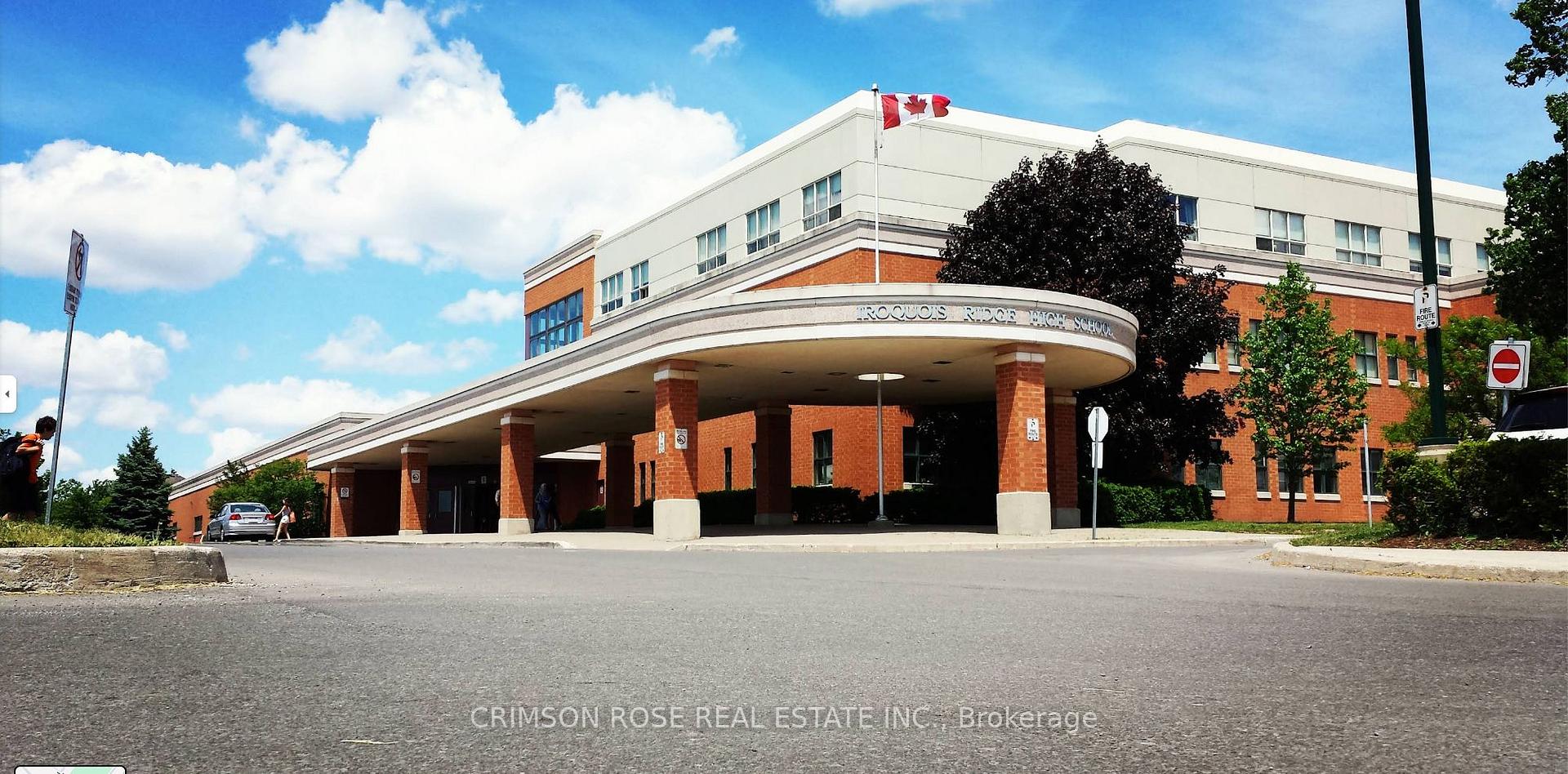 Iroquois Ridge High School’s red-brick entrance beneath a covered drive, with a Canadian flag flying above.