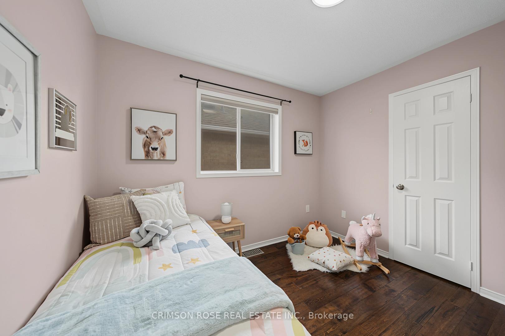 Child’s bedroom with a single bed, plush toys, pale pink walls, and dark wood flooring.