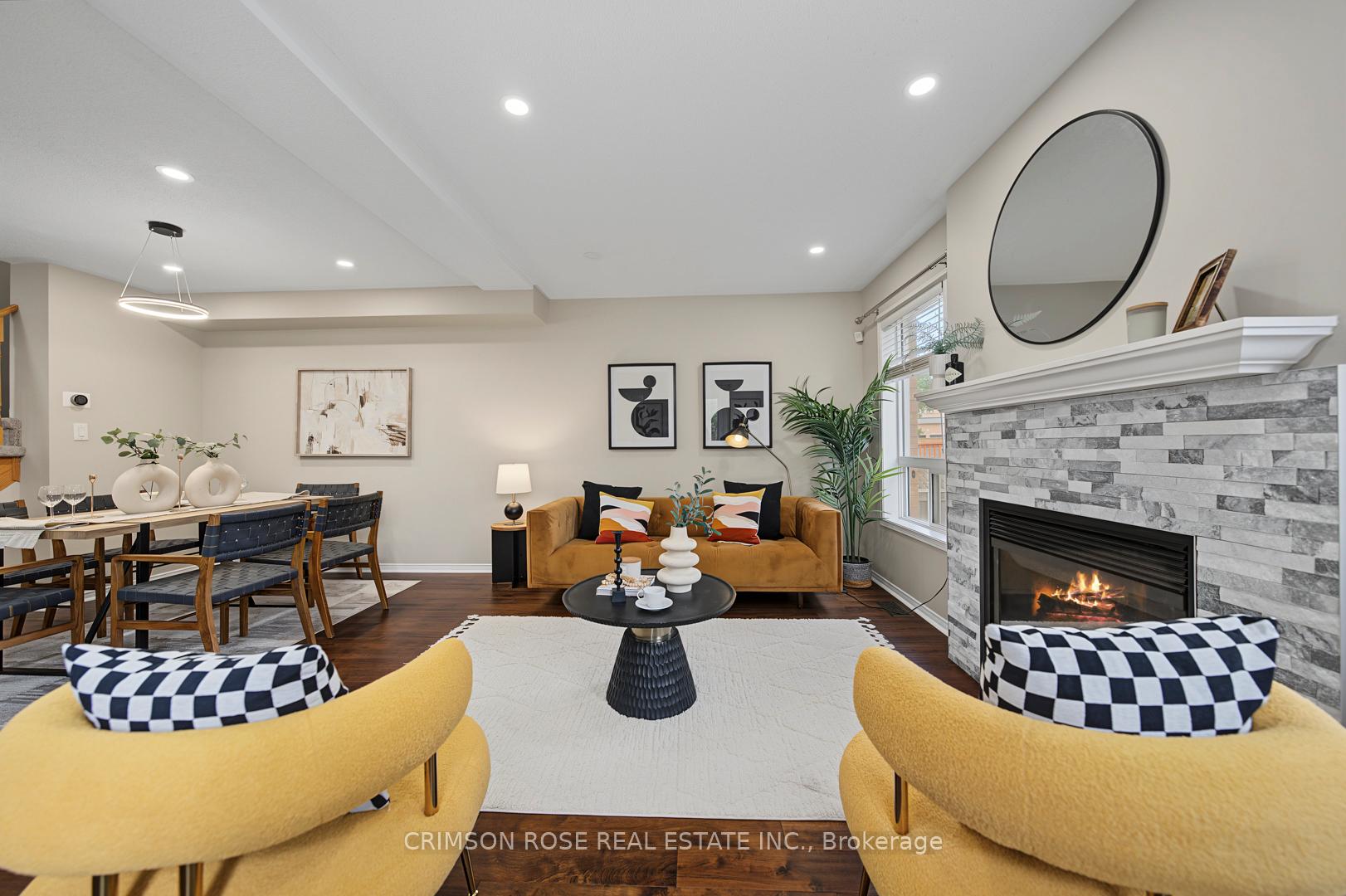 Staged living room with a gray stone fireplace, mustard seating, and an adjoining dining area.