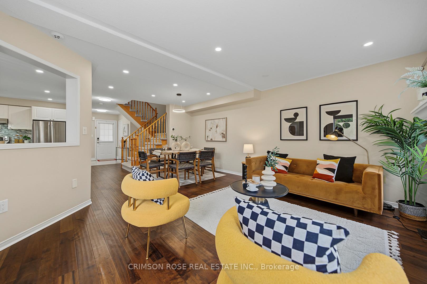 Staged living and dining room with mustard-yellow seating, dark hardwood floors, and a wood-railed staircase.