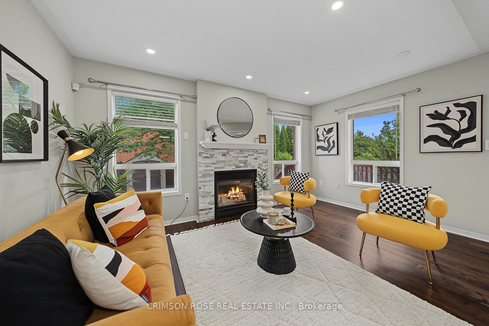 Staged living room with a stone fireplace, mustard-yellow seating, and large windows overlooking greenery.