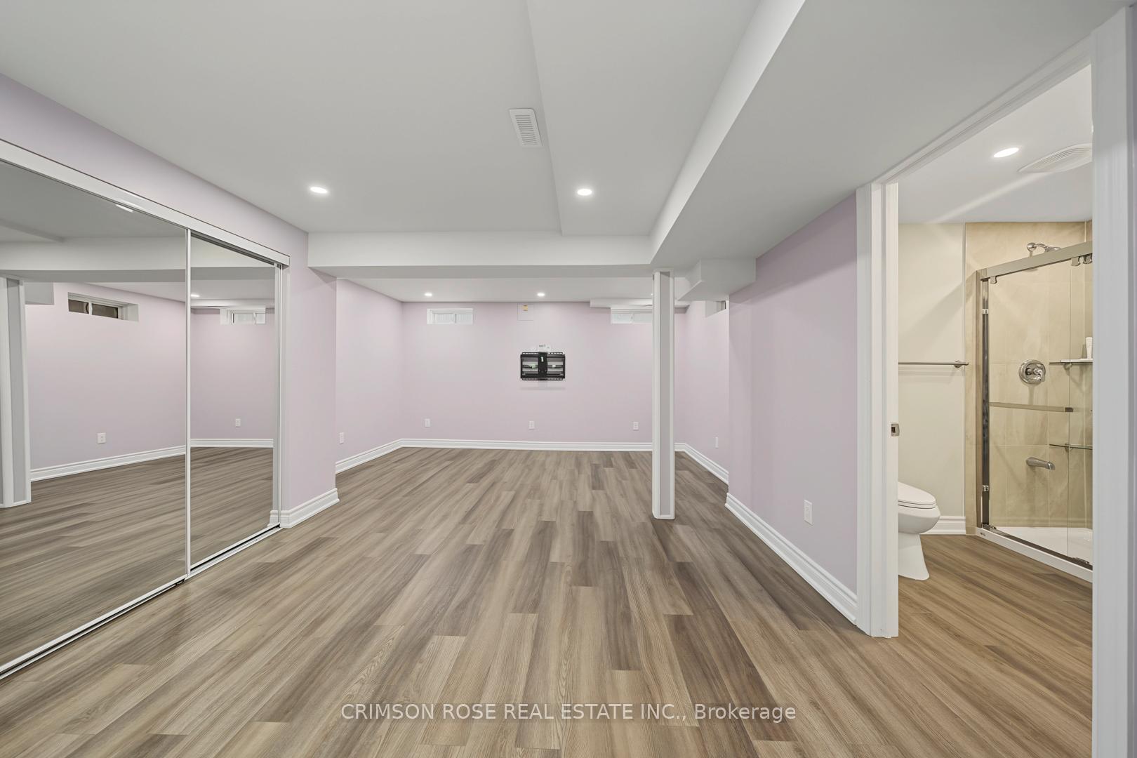 Finished basement room with mirrored closet doors and an adjoining bathroom with a glass shower.