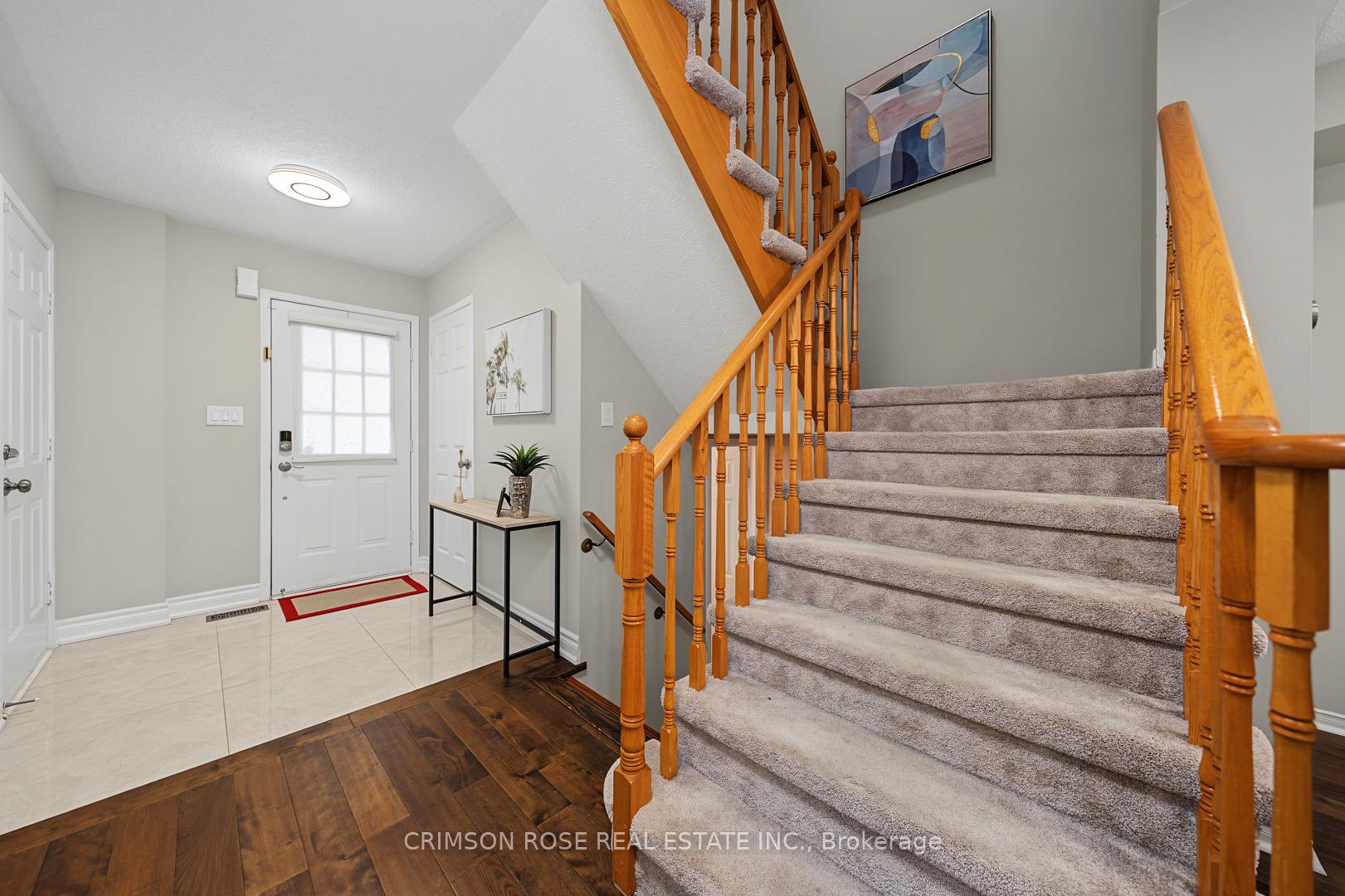 Entryway with a white front door and tiled floor beside a carpeted staircase with wooden railings.