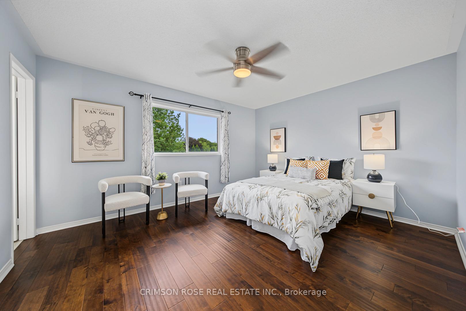 Furnished bedroom with a botanical-patterned bed, two chairs, and a window overlooking leafy trees.