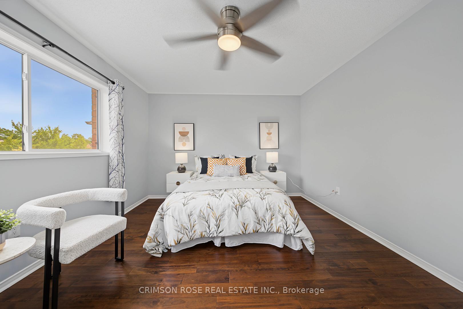 Staged bedroom with a centered bed, dark hardwood floors, large window, and ceiling fan.