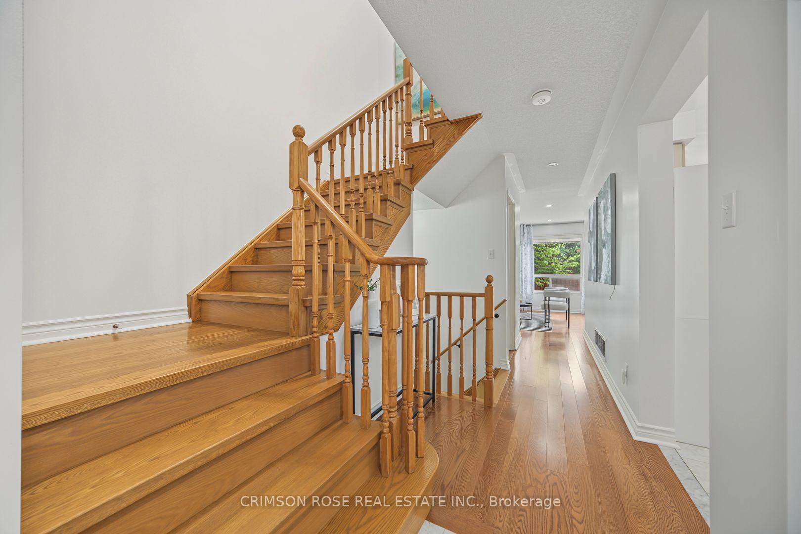 Oak staircase with turned wood railings beside a bright hardwood-floored hallway.