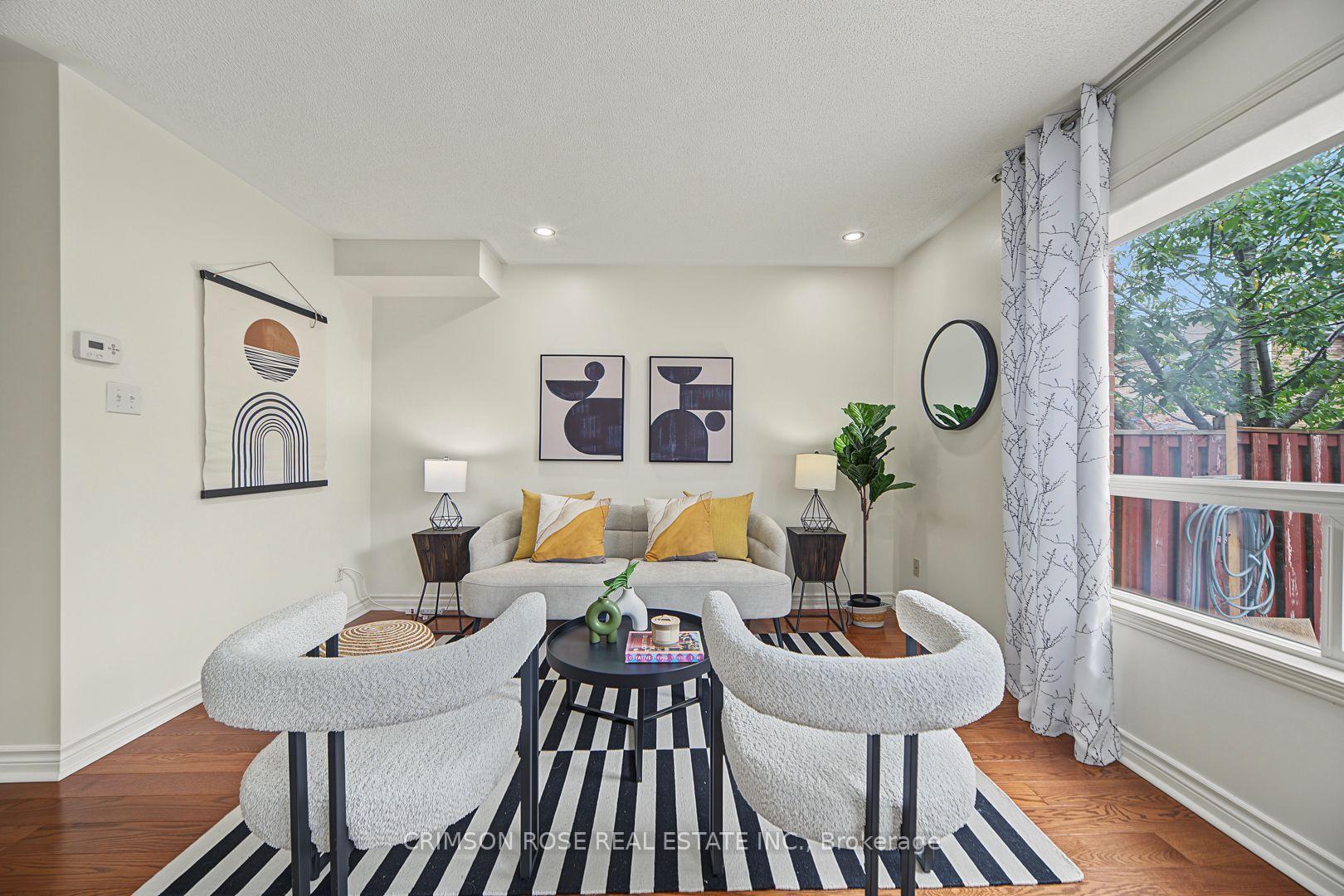 Staged living room with a gray sofa, boucle chairs, striped rug, and large windows overlooking a fenced yard.