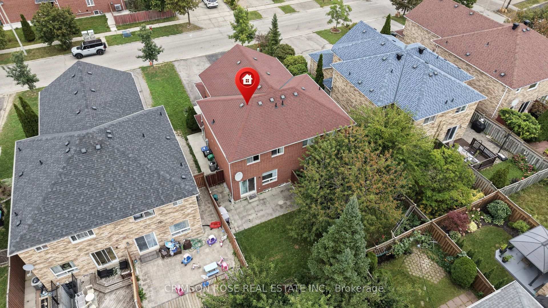 Aerial view of a red-brick house with a location pin and fenced, tree-filled backyard.