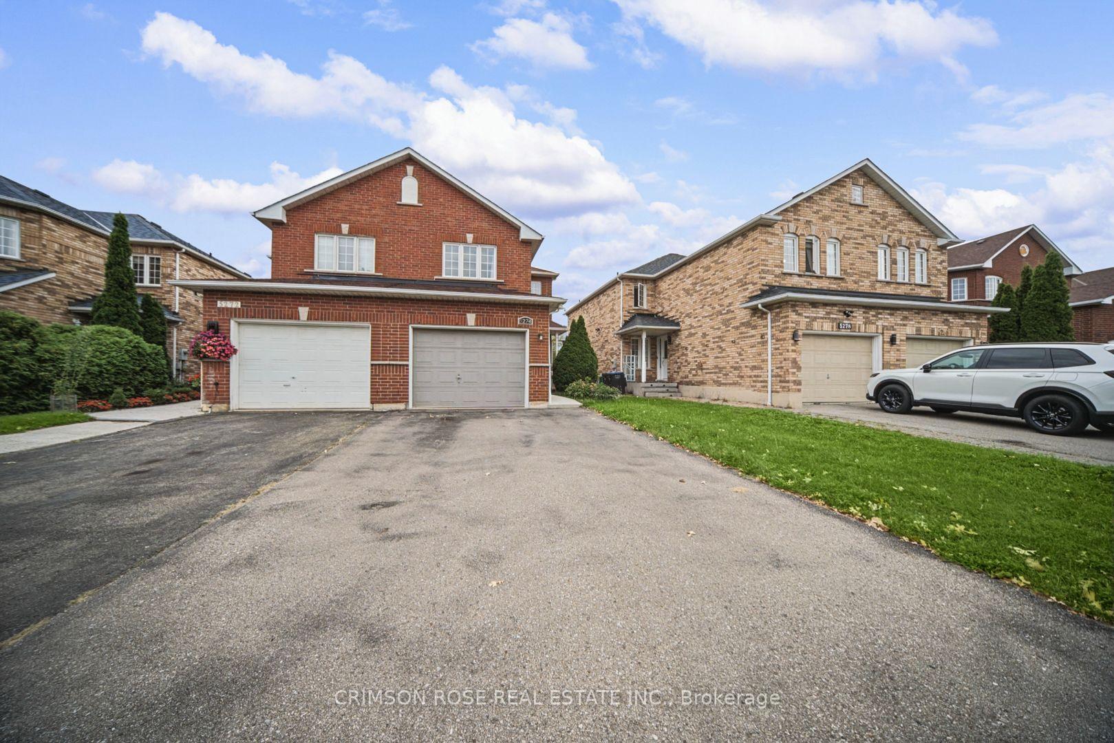 Two-storey red brick house with two garage doors and a wide driveway.
