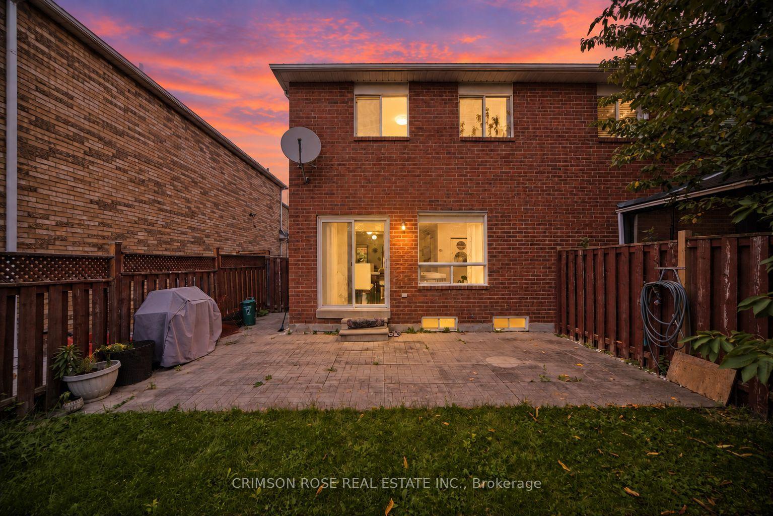 Red-brick home’s fenced backyard patio at sunset, with warm light glowing through the windows.