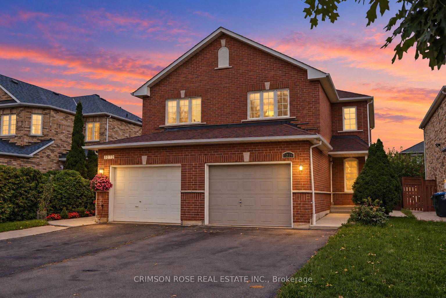 Two-story red-brick house with twin garage doors and glowing windows at dusk.