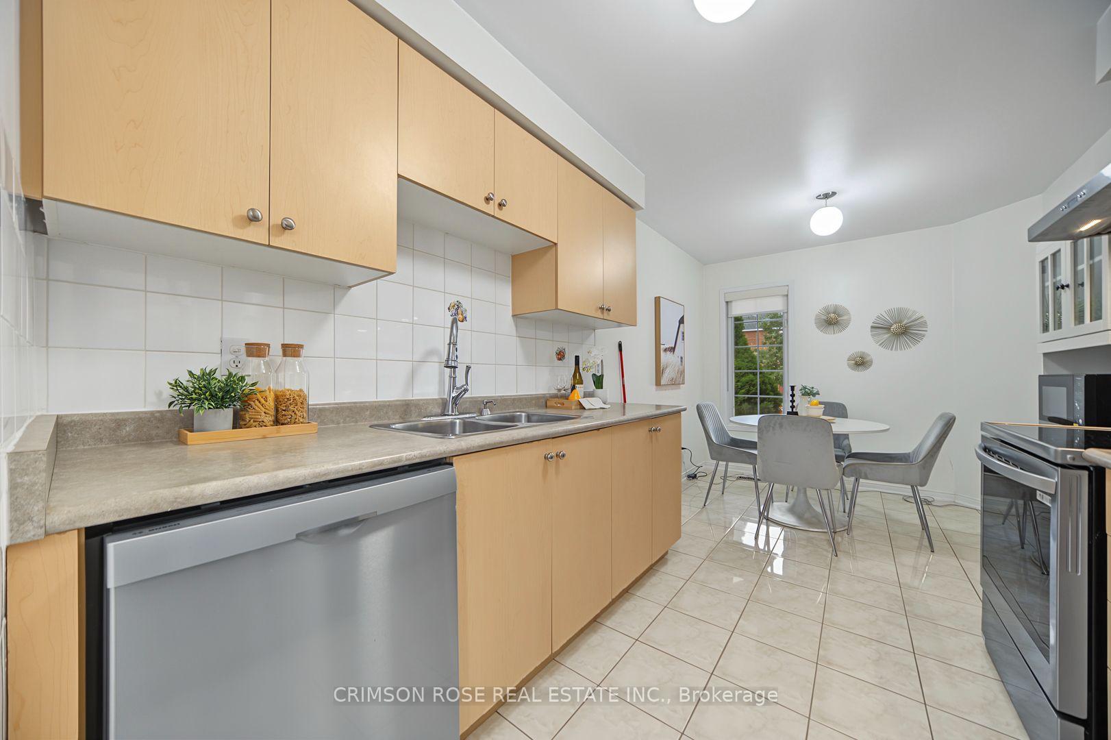 Kitchen with light wood cabinets and stainless appliances opening to a dining area with a round table.