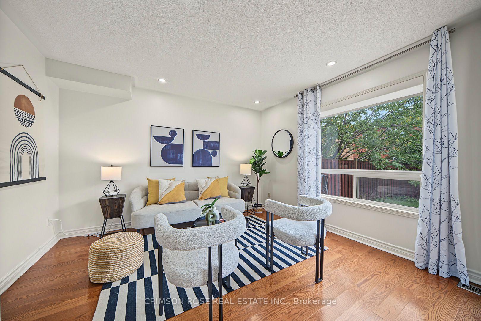 Staged living room with a gray sofa, sculptural chairs, striped rug, and large window overlooking trees.