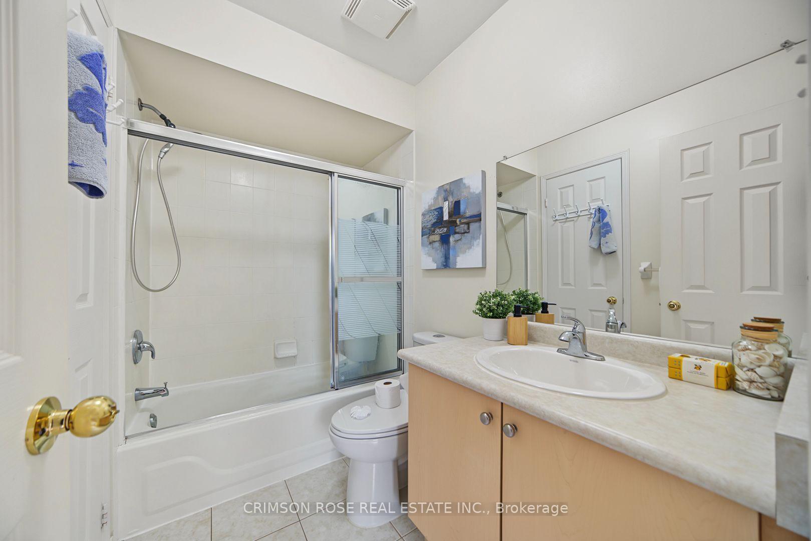 Bathroom with a glass-enclosed tub, toilet, and light wood vanity with an oval sink.