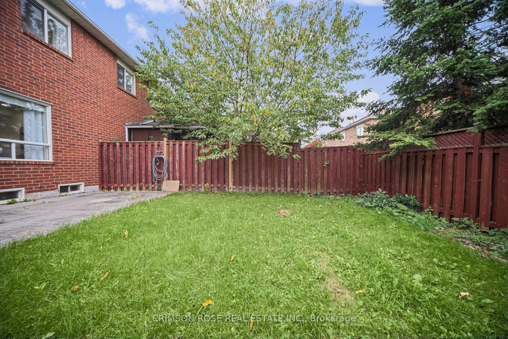 Backyard with a broad lawn, mature trees, and a reddish-brown wooden fence beside a red-brick house.