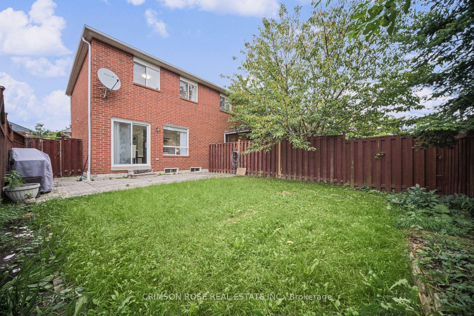 Two-story brick home viewed from a fenced backyard with a lawn and mature tree.