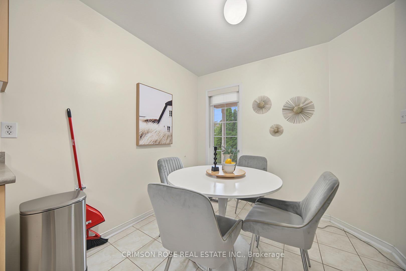 Dining area with a round white table, gray chairs, and a window overlooking greenery.