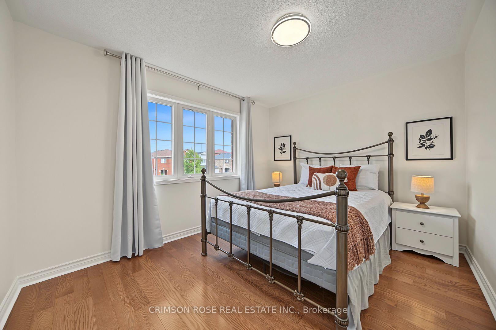 Staged bedroom with a dark metal four-poster bed, rust-colored accents, hardwood floors, and a large window.