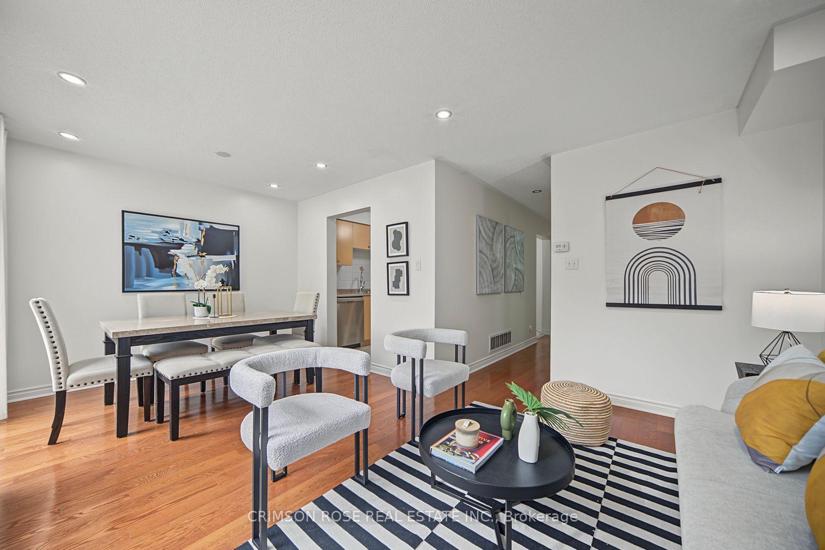 Open-concept dining and living room with hardwood floors, upholstered chairs, and a black-and-white geometric rug.