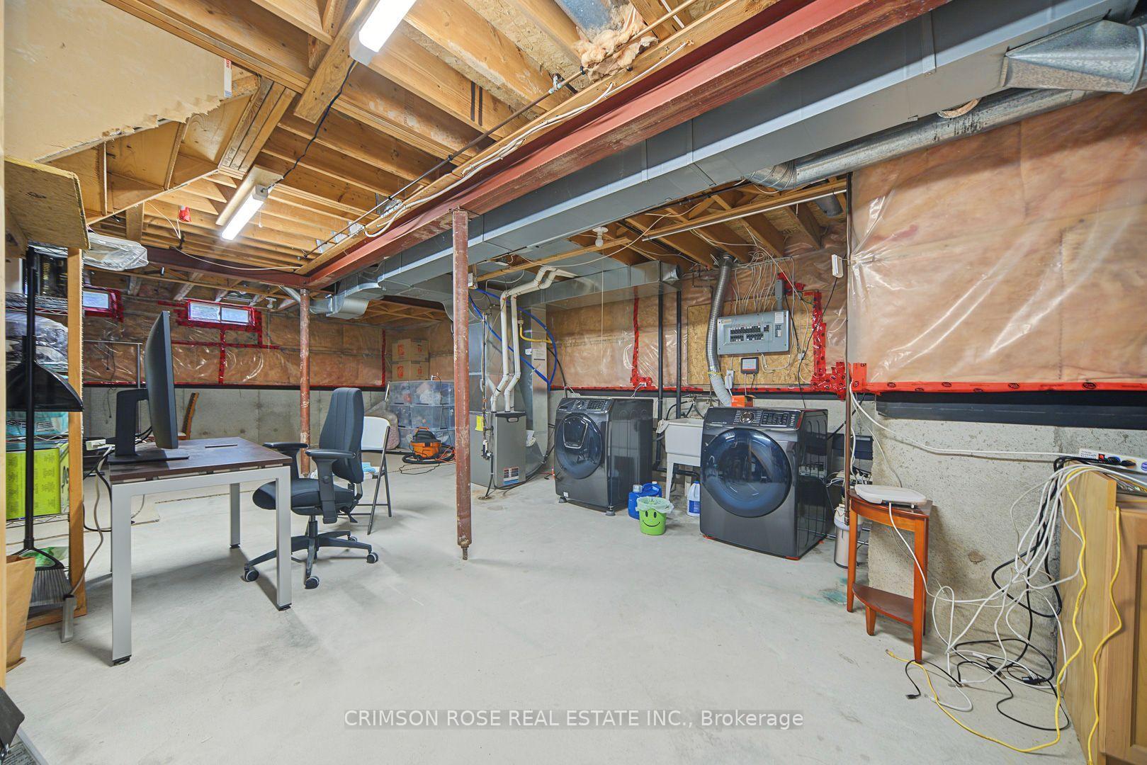 Unfinished basement with exposed ceiling framing, laundry machines, and a small desk workspace.