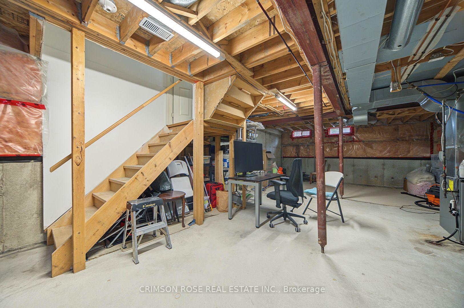 Unfinished basement with exposed joists, ductwork, a wooden staircase, and a desk area.