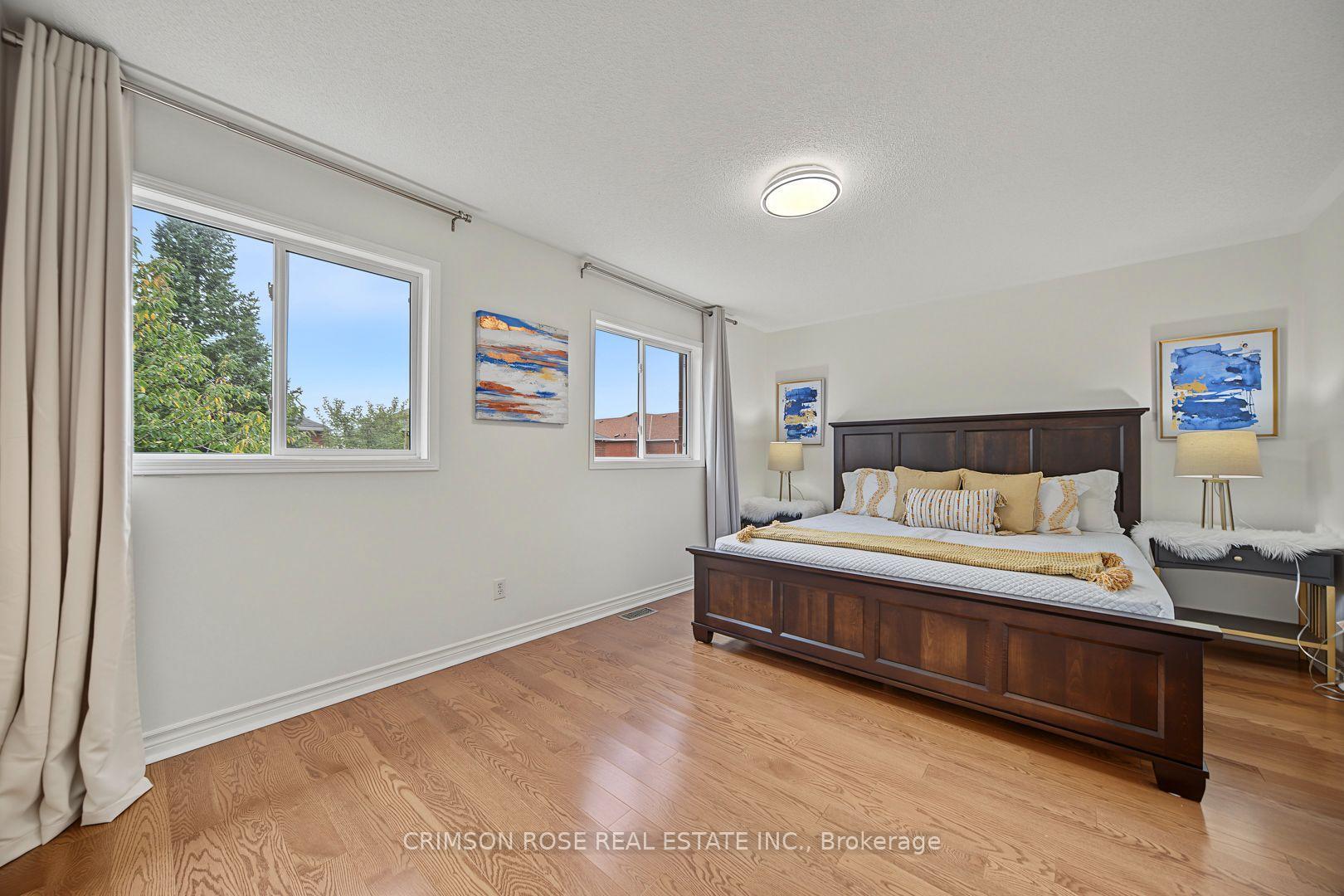 Furnished bedroom with a dark wood bed, hardwood floors, and two large curtained windows.