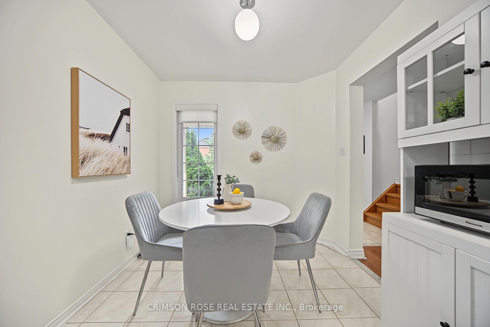 Dining area with a round white table, gray chairs, and a window overlooking greenery.